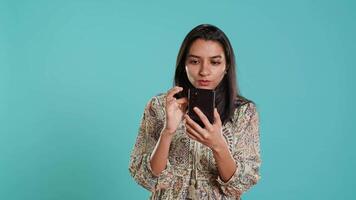 mulher rolagem em Smartphone tela, fazendo conectados compras, espantado de lindo roupas. retrato do relaxado pessoa navegando Internet sites, exclamando dentro espanto, estúdio fundo, Câmera uma video