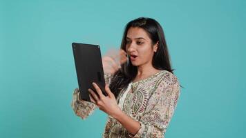 Upbeat woman having friendly conversations during teleconference meeting using tablet, studio background. Person having fun catching up with mates during online videocall on digital device, camera A video