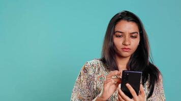 Indian woman discussing with best friend over telephone call using smartphone. Cheerful person talking with mate in phone call using cellphone, isolated over studio background, camera B video