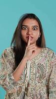 Vertical Annoyed indian woman doing shushing hand gesturing, irritated by noise, having negative mood. Person placing finger on lips, doing quiet sign gesture, isolated over studio background, camera A video