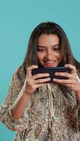 verticale Contentissimo persona giocando intenso mobile gioco, festeggiare vincita, studio sfondo. estatico donna eccitato dopo essere vittorioso nel smartphone video gioco, sconfiggere tutti nemici, telecamera un'