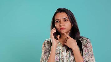 Indian woman talking with friends in phone call using smartphone, isolated over studio background. Portrait of person having discussion with mate during telephone call, camera B video