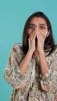 Vertical Anxious indian woman covering face with palms, worried about future, isolated over studio background. Tense person shocked by troubling news, gasping, feeling distressed, camera A video