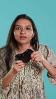 Vertical Focused woman playing videogames with motion controlled joystick, studio background. Indian gamer participating in online multiplayer racing game using gyroscope function on gamepad, camera A video