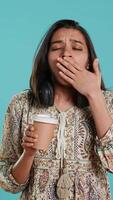 Vertical Woman suffering from insomnia yawning, sipping coffee to gain energy and get rid of pain. Tired person feeling drowsy after sleepless night, drinking caffeinated beverage, studio background, camera A video