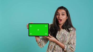 Energetic salesman doing influencer marketing using green screen tablet, studio background. Lively woman reviewing product, holding empty copy space mockup digital device, camera A video