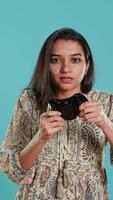 Vertical Cheerful woman playing videogames with controller, studio background. Indian gamer smiling, having fun by participating in PvP online multiplayer game using console system, camera A video