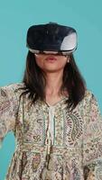 Vertical Indian woman wearing virtual reality headset, doing swiping gestures. Technology enthusiast using high tech futuristic modern VR gadget, isolated over studio background, camera A video