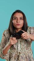 Vertical Upset woman showing thumbs down sign gesturing holding controller after being defeated in videogames. Displeased indian person doing rejection hand gesture after losing, studio background, camera A video