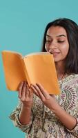 Vertical Woman reading interesting book, enjoying hobby, being entertained, isolated over studio background. Indian lady with intriguing novel in arms enjoying relaxation time, camera A video