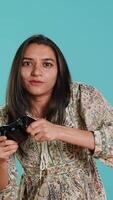 Vertical Gamer annoyed after losing online multiplayer videogame, being defeated by rival players. Indian woman upset after seeing game over message, holding controller, studio background, camera A video