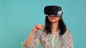 indiano mulher vestindo virtual realidade fone de ouvido, fazendo batendo gestos. tecnologia entusiasta usando Alto tecnologia futurista moderno vr engenhoca, isolado sobre estúdio fundo, Câmera b video