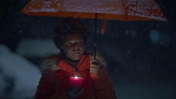 Jeune africain femme permanent sur rue à nuit pendant neige tomber avec parapluie video