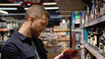 un hombre toma alcohólico bebidas desde el supermercado estante. compras para alcohol en el Tienda video