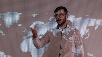 Confident professional speaker presents report problem of global warming and sources of renewable energy at meeting room with world map on background video