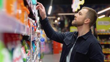 Young cheerful positive male customer making purchases in supermarket, buying household chemicals video