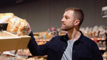jovem homem escolhendo pão às supermercado. escolhendo Comida a partir de estante dentro supermercado. padaria, mercearia lojas video