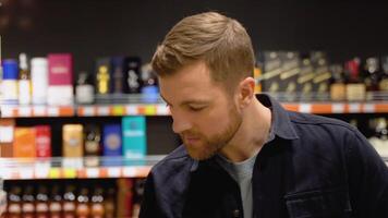 une homme prend alcoolique les boissons de le supermarché étagère. achats pour de l'alcool dans le boutique video