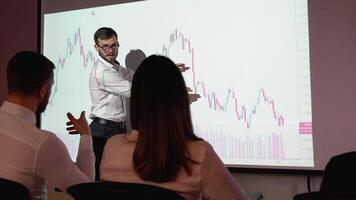 Young trader presents cryptocurrency investment strategy for group of investors. Wall TV showing big data analysis, infographics, stock market information, trends video