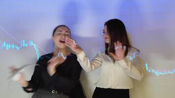 twee grappig vrouw handelaren dans tegen de achtergrond van cryptogeld tabel video