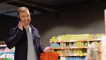 giovane uomo la scelta broccoli a supermercato. un' uomo fare drogheria shopping nel supermercato. chiamata il suo moglie chiede che cosa verdure per scegliere video