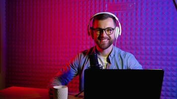 Content creator man host streaming his a podcast on laptop with headphones and condenser microphone interview guest conversation at home broadcast studio video