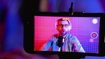 gefocust schot Aan smartphone opname Kaukasisch blogger pratend op zoek Bij camera gedurende online podcasten. inhoud Schepper streaming online uitzending, blogger bespreken vervelend hoofdtelefoons video