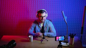 Content creator man host streaming his a podcast on smartphone with headphones and condenser microphone interview guest conversation at home broadcast studio. Male blogger recording voice over radio video