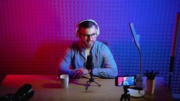 Content creator man host streaming his a podcast on smartphone with headphones and condenser microphone interview guest conversation at home broadcast studio. Male blogger recording voice over radio video