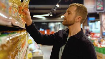 A young man chooses oliy in a supermarket. Choosing food from a shelf in a supermarket video