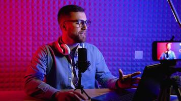 Content creator man host streaming his a podcast on laptop with headphones and condenser microphone interview guest conversation at home broadcast studio. Male blogger recording voice over radio video