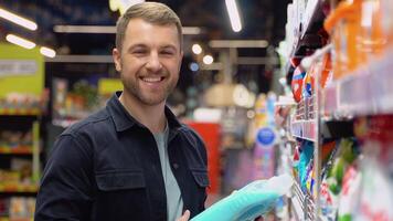 Young cheerful positive male customer making purchases in supermarket, buying household chemicals video