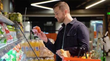 joven hombre elegir tomate a supermercado. elegir comida desde estante en supermercado video