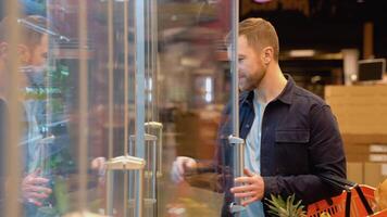 Caucasian man shopping in beverage section at supermarket. A man doing shopping at market while buying cold drink. Handsome guy holding shopping basket reading nutritional values of product video