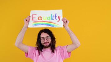ung aktivist leende Lycklig roligt Gay man i rosa t-shirt innehav en protest tecken under en HBTQ stolthet parad isolerat på gul bakgrund studio. människor HBTQ livsstil begrepp video