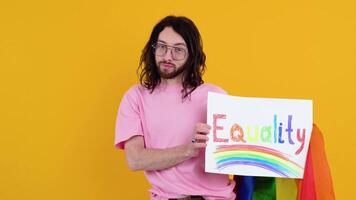 Young activist smiling happy fun gay man in pink t-shirt holding a protest sign during a LGBT pride parade isolated on yellow background studio. People lgbt lifestyle concept video