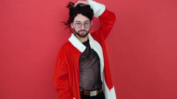 Young smiling happy cheerrful gay man wearing mesh t-shirt and Christmas Santa Claus suit isolated on bright red color background studio portrait. Concept diversity, transsexual, and freedom video