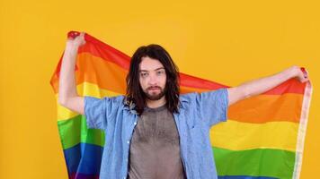 Young activist smiling happy fun gay man in mesh t-shirt waving hold rainbow flag isolated on yellow background studio. People lgbt lifestyle concept video