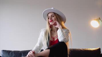 un' donna con tinti capelli e trucco nel un' cappello, bianca giacca e rosso reggiseno pose nel il studio. moda tiro concetto video