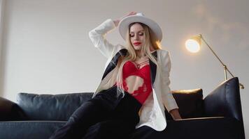 een vrouw met geverfd haar- en bedenken in een hoed, wit jasje en rood beha poses in de studio. mode het schieten concept video
