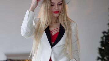 A woman with dyed hair and make-up in a hat, white jacket and red bra poses in the studio. Fashion shooting concept video