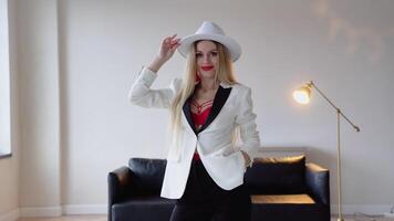 A woman with dyed hair and make-up in a hat, white jacket and red bra poses in the studio. Fashion shooting concept video
