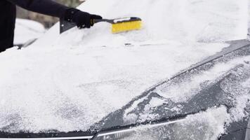 A young man in close-up cleans his car after a snowfall on a frosty day. Cleaning and clearing the car from snow on a winter day. Snowfall, and a severe snowstorm in winter video