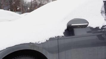 A young man in close-up cleans his car after a snowfall on a frosty day. Cleaning and clearing the car from snow on a winter day. Snowfall, and a severe snowstorm in winter video