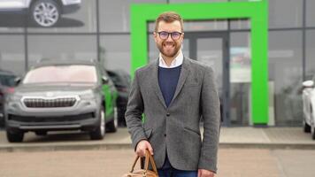 gracioso elegante hombre sonriente cerca un coche concesión. un hombre compra un nuevo eléctrico coche video