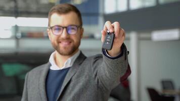 Positive seller smiling for camera and demonstrating keys while standing near new vehicle in showroom video