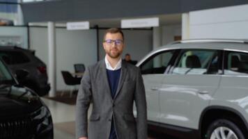 Caucasian man in glasses and suit coming to the camera and smiling in car dealership video