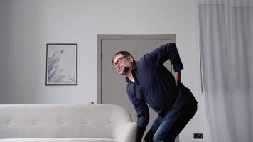 Senior man suffering from backpain while lifting sofa in living room. Healthcare concept video