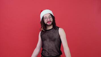 Young smiling happy cheerrful gay man wearing mesh t-shirt and Christmas Santa Claus red hat isolated on bright red color background studio portrait. Lifestyle lgbtq pride concept video