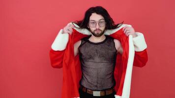 Young smiling happy transsexual man wearing mesh t-shirt and Christmas Santa Claus suit isolated on bright red color background studio portrait. Lifestyle lgbtq pride concept video